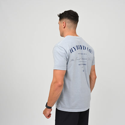 A man wearing a light blue washed cotton t-shirt with navy blue HYBRYD graphic text on the back, shown from a rear three-quarter view against a plain light gray background.