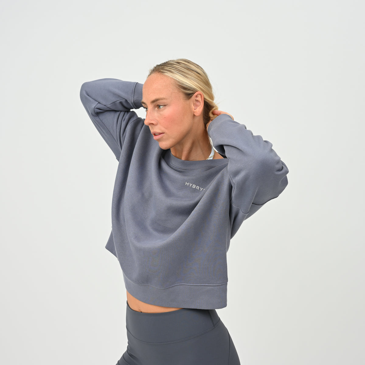 Women’s HYBRYD oversized organic cotton sweatshirt in washed slate grey, with chest logo, styled with dark grey gym leggings.