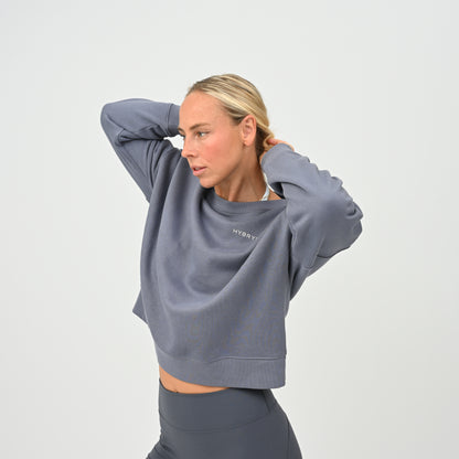 Women’s HYBRYD oversized organic cotton sweatshirt in washed slate grey, with chest logo, styled with dark grey gym leggings.