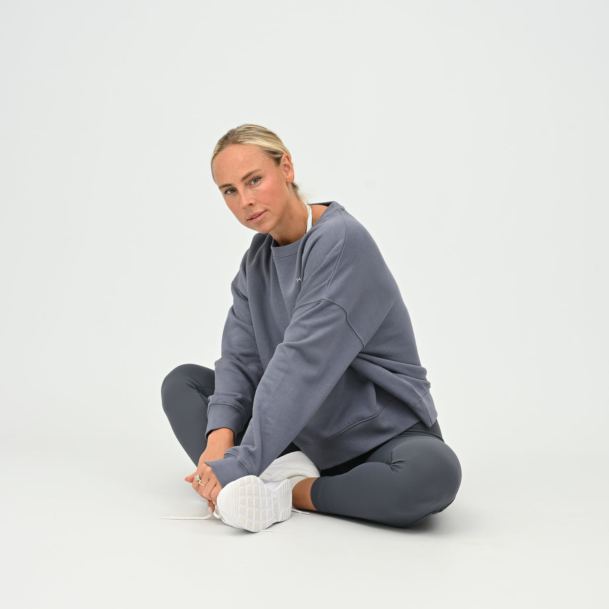 Women’s HYBRYD oversized organic cotton sweatshirt in washed slate grey, with chest logo, styled with dark grey gym leggings.