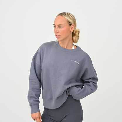 Women’s HYBRYD oversized organic cotton sweatshirt in washed slate grey, with chest logo, styled with dark grey gym leggings.