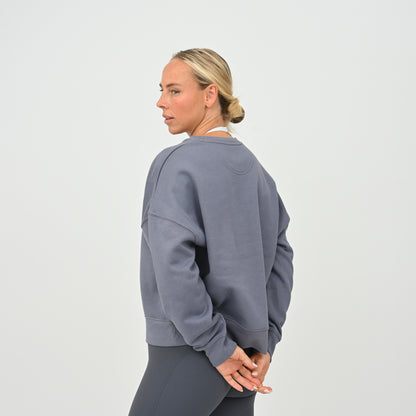 Women’s HYBRYD oversized organic cotton sweatshirt in washed slate grey, with chest logo, styled with dark grey gym leggings.
