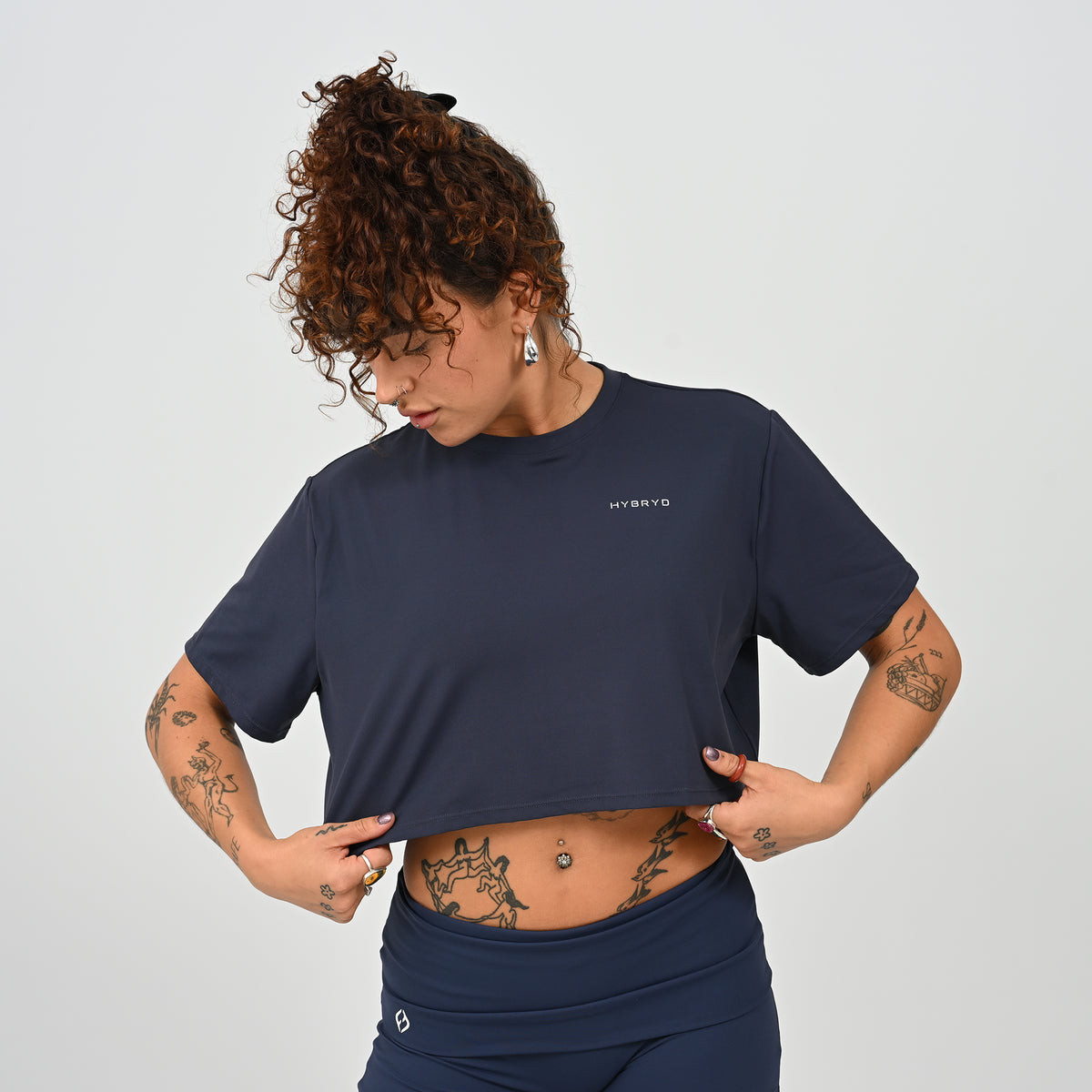 A training tee, oversized, cropped fit in Navy colour. HYBRYD branding on upper left chest. Worn by a gym girl. From activewear brand Hybryd.