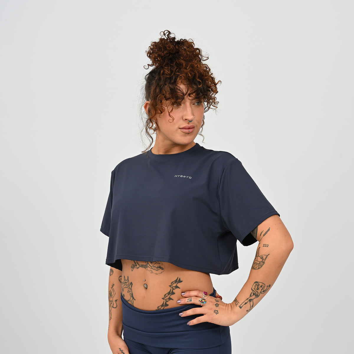A training tee, oversized, cropped fit in Navy colour. HYBRYD branding on upper left chest. Worn by a gym girl. From activewear brand Hybryd.