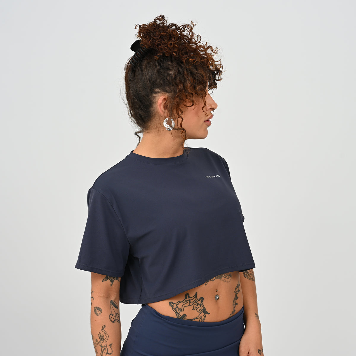 A training tee, oversized, cropped fit in Navy colour. HYBRYD branding on upper left chest. Worn by a gym girl. From activewear brand Hybryd.