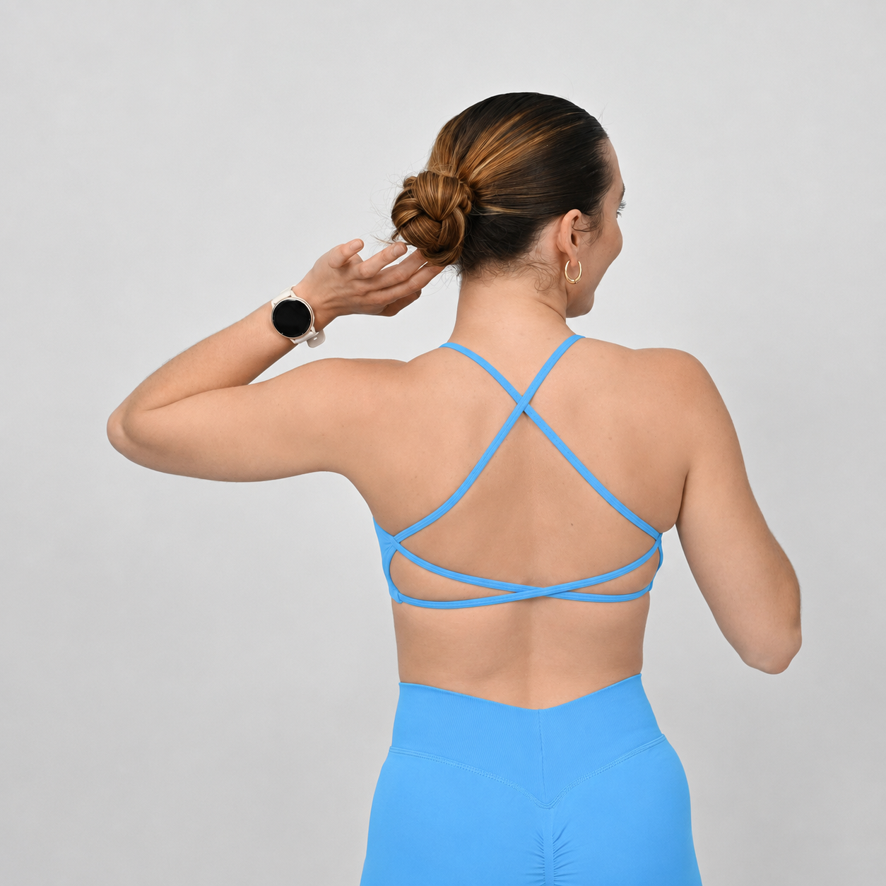 A woman shown from the back wearing a bright blue strappy Hybryd sports bra and matching blue scrunch bum shorts against a light gray studio background.