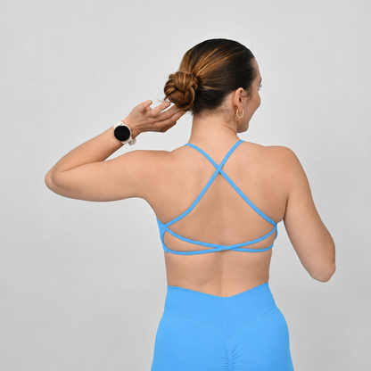 A woman shown from the back wearing a bright blue strappy Hybryd sports bra and matching blue scrunch bum shorts against a light gray studio background.