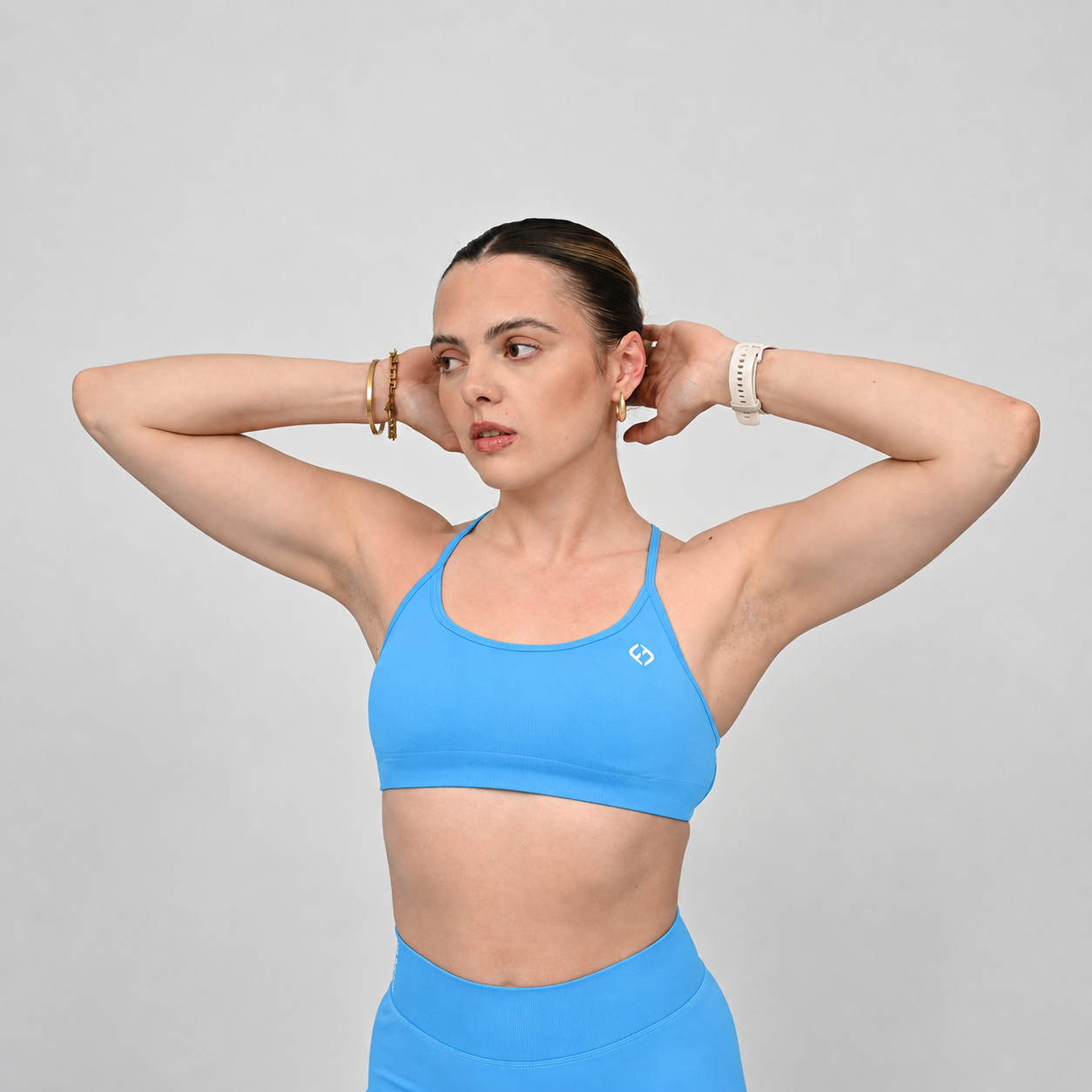 A woman posing in a bright blue athletic sports bra and matching high-waisted bootie shorts against a solid light gray background.