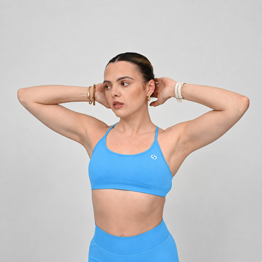 A woman posing in a bright blue athletic sports bra and matching high-waisted bootie shorts against a solid light gray background.