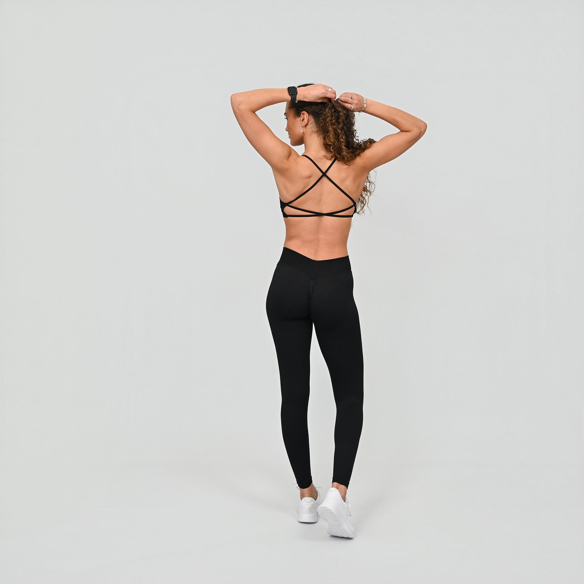 Girl wearing black Hybryd equinox leggings that have a v-dip rear waist and a scrunch bum. Shot from the rear, she wears a minimal sports bra. From activewear brand Hybryd