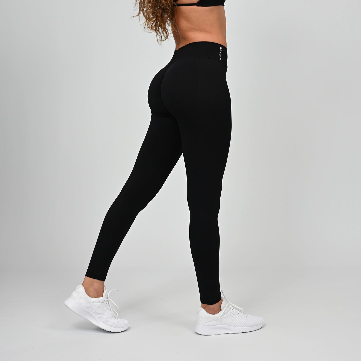 Girl wearing black Hybryd equinox leggings that have a v-dip rear waist and a scrunch bum. From activewear brand Hybryd