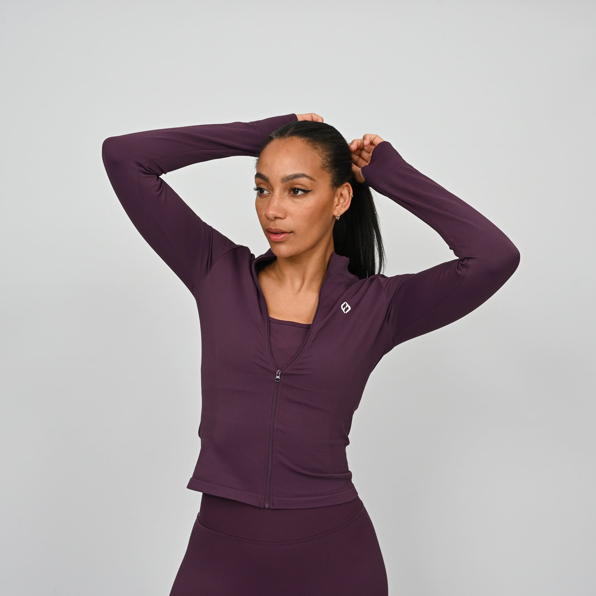 Woman wearing a purple athletic gym set with a zip on a gray background