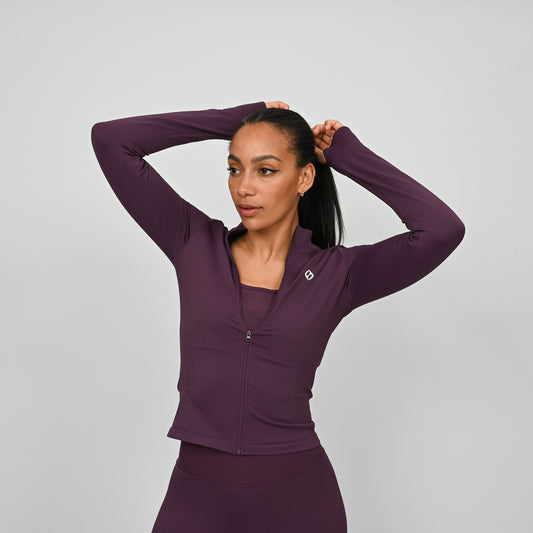 Woman wearing a purple athletic gym set with a zip on a gray background