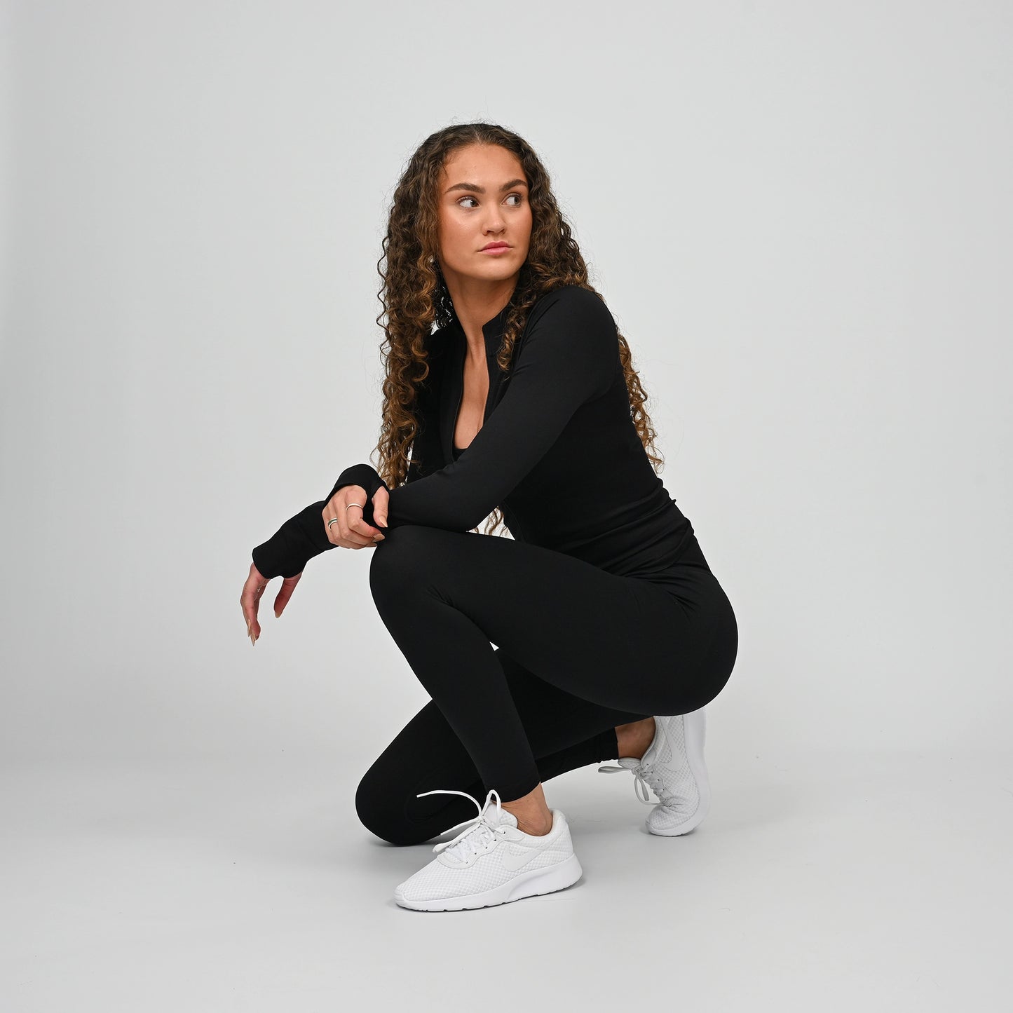 Woman in black workout gym outfit squatting on a plain background