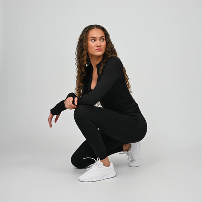 Woman in black workout gym outfit squatting on a plain background