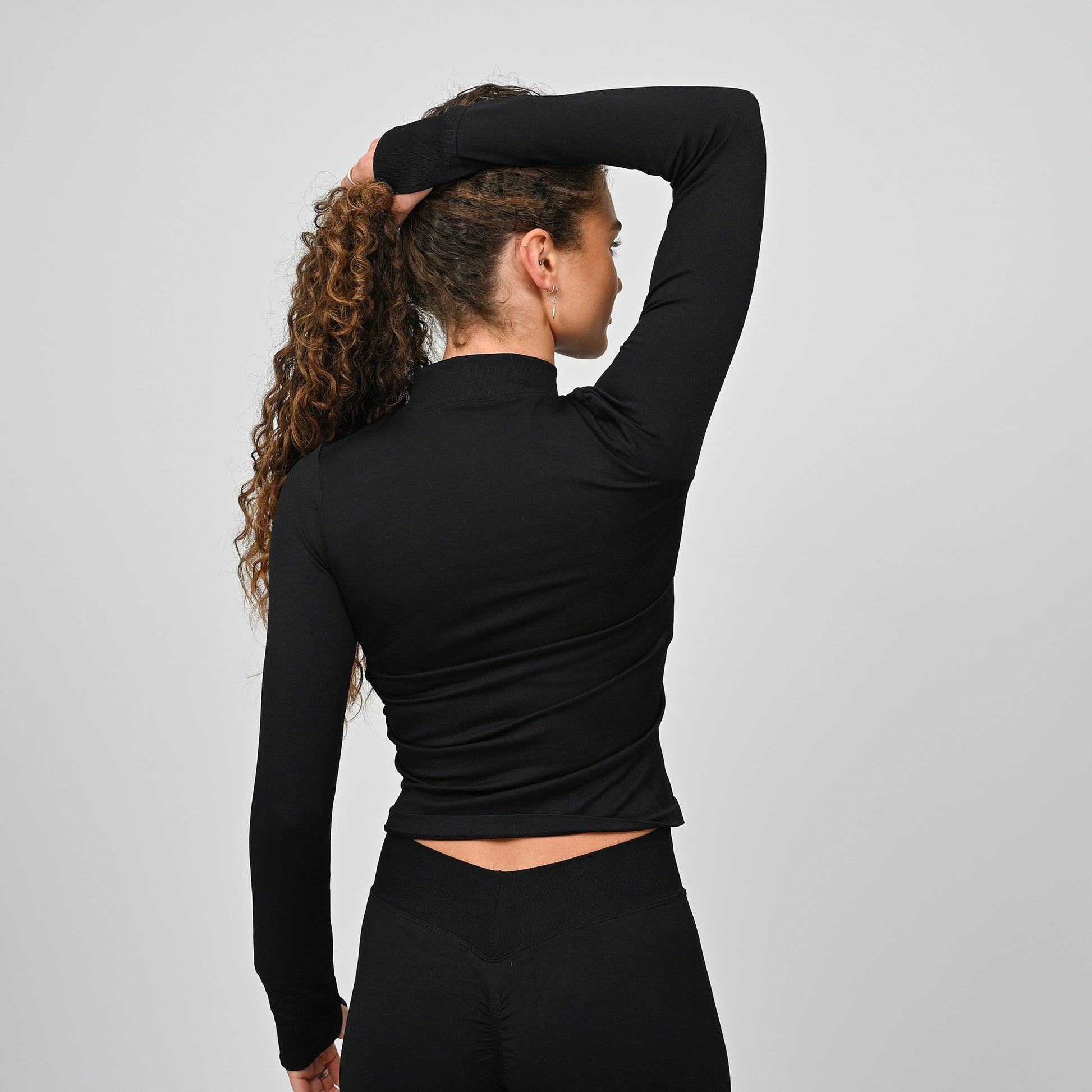 Athlete wearing a black long-sleeve training top with a high neckline on a gray background