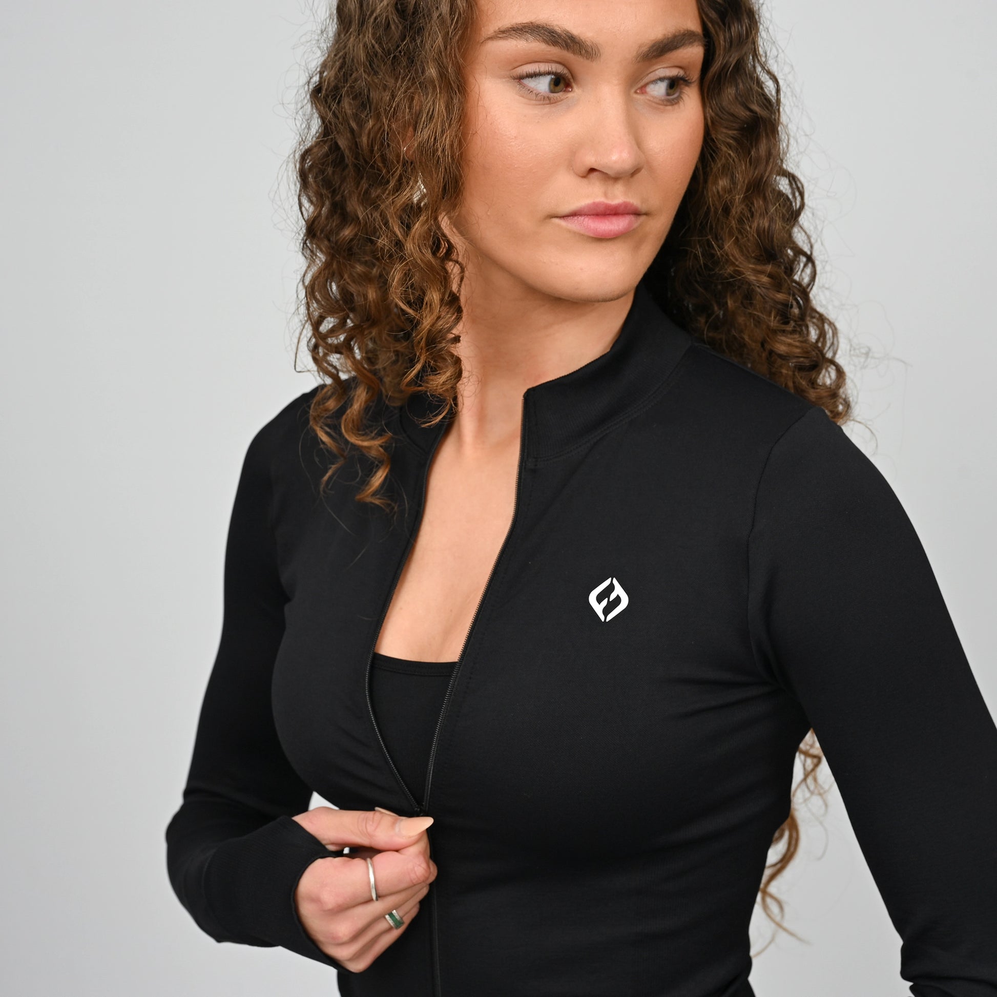 Woman wearing a black zipped gym jacket with a logo on a gray background