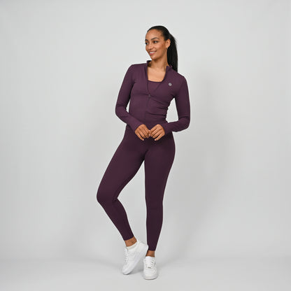 Woman wearing a purple athletic fitted jacket and leggings gym outfit on a gray background