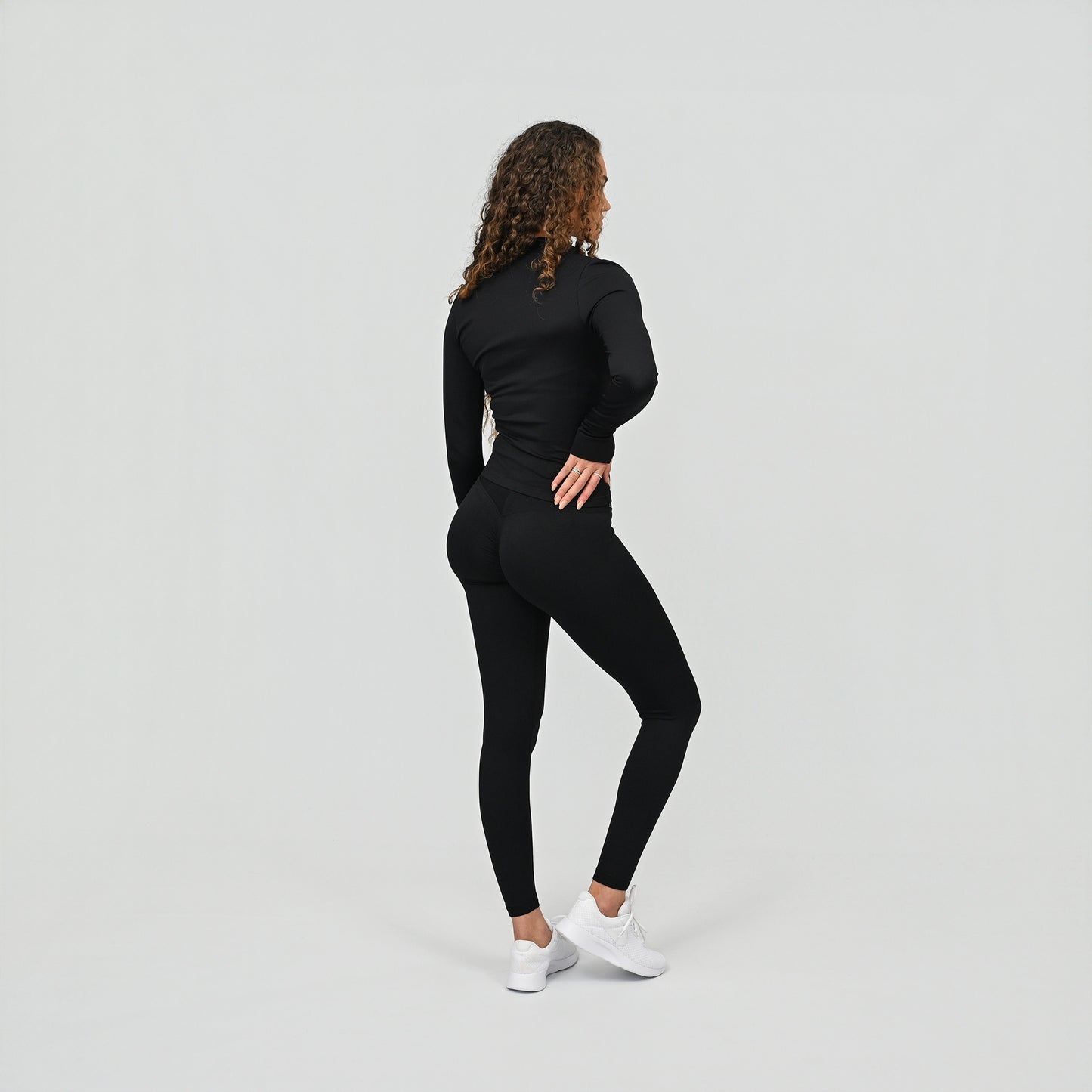 Person wearing a black outfit with scrunch bum leggings and a zip up gym top on a light gray background