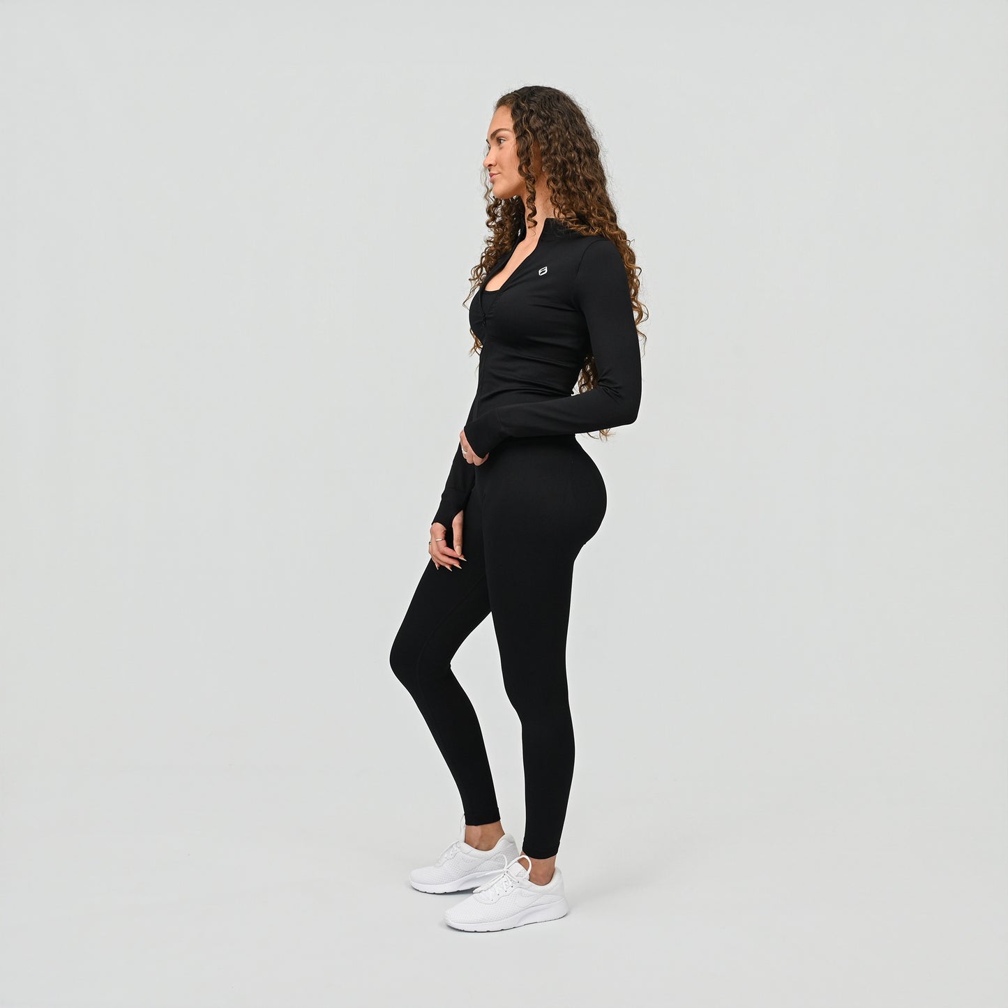 Woman wearing a black long-sleeve top and cinched leggings on a light gray background