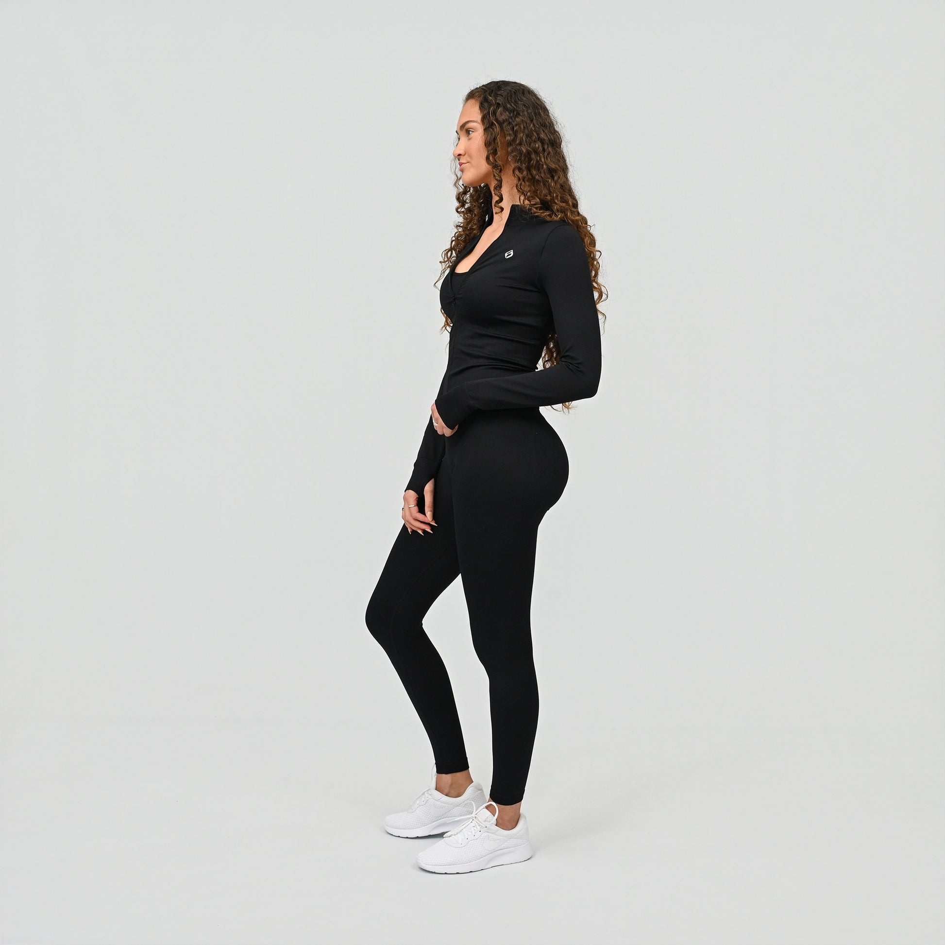 Woman wearing a black long-sleeve top and cinched leggings on a light gray background