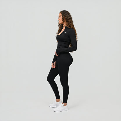 Woman wearing a black long-sleeve top and cinched leggings on a light gray background