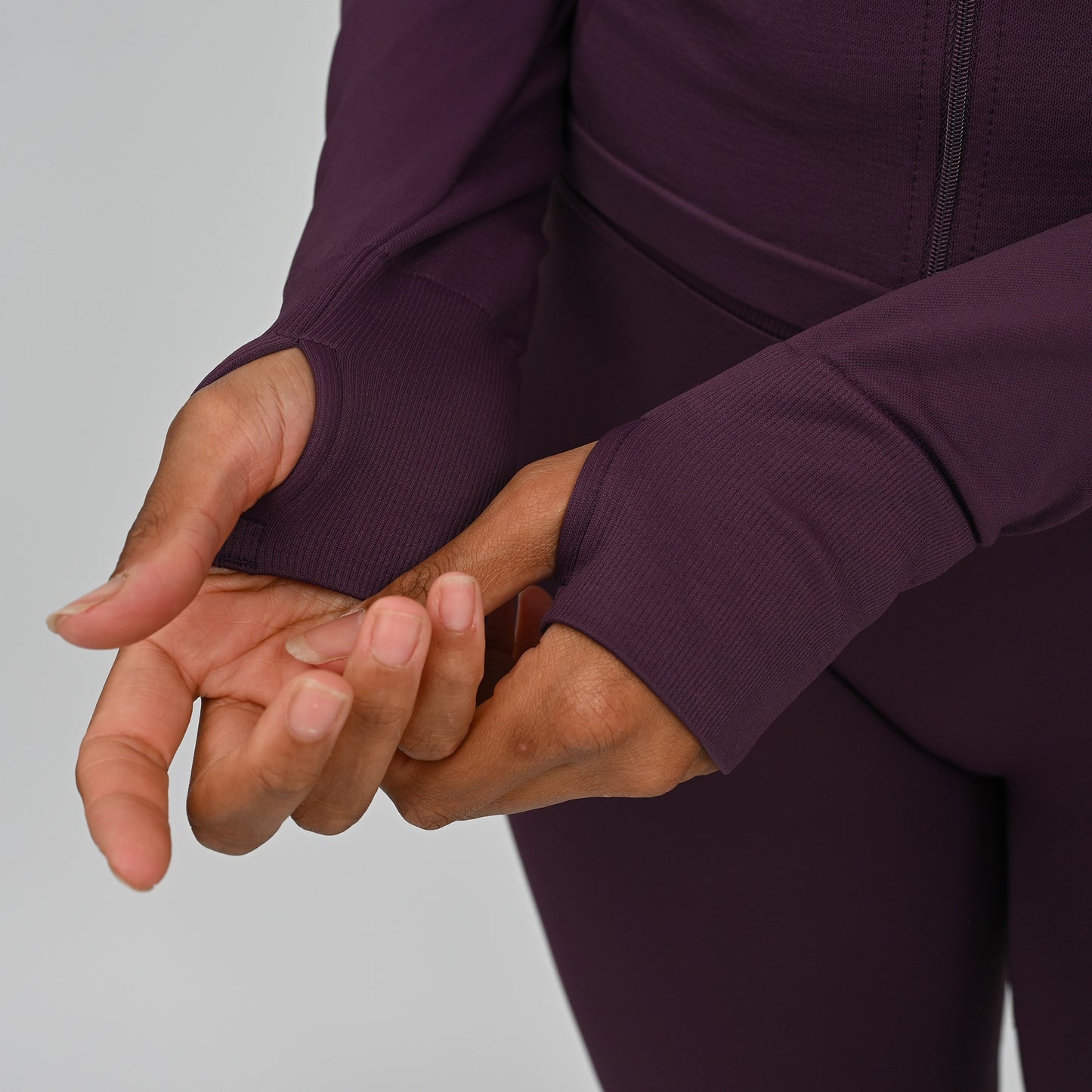 Close-up of a crossfit athlete wearing a dark purple athletic outfit with thumb holes a plain background