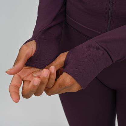 Close-up of a crossfit athlete wearing a dark purple athletic outfit with thumb holes a plain background