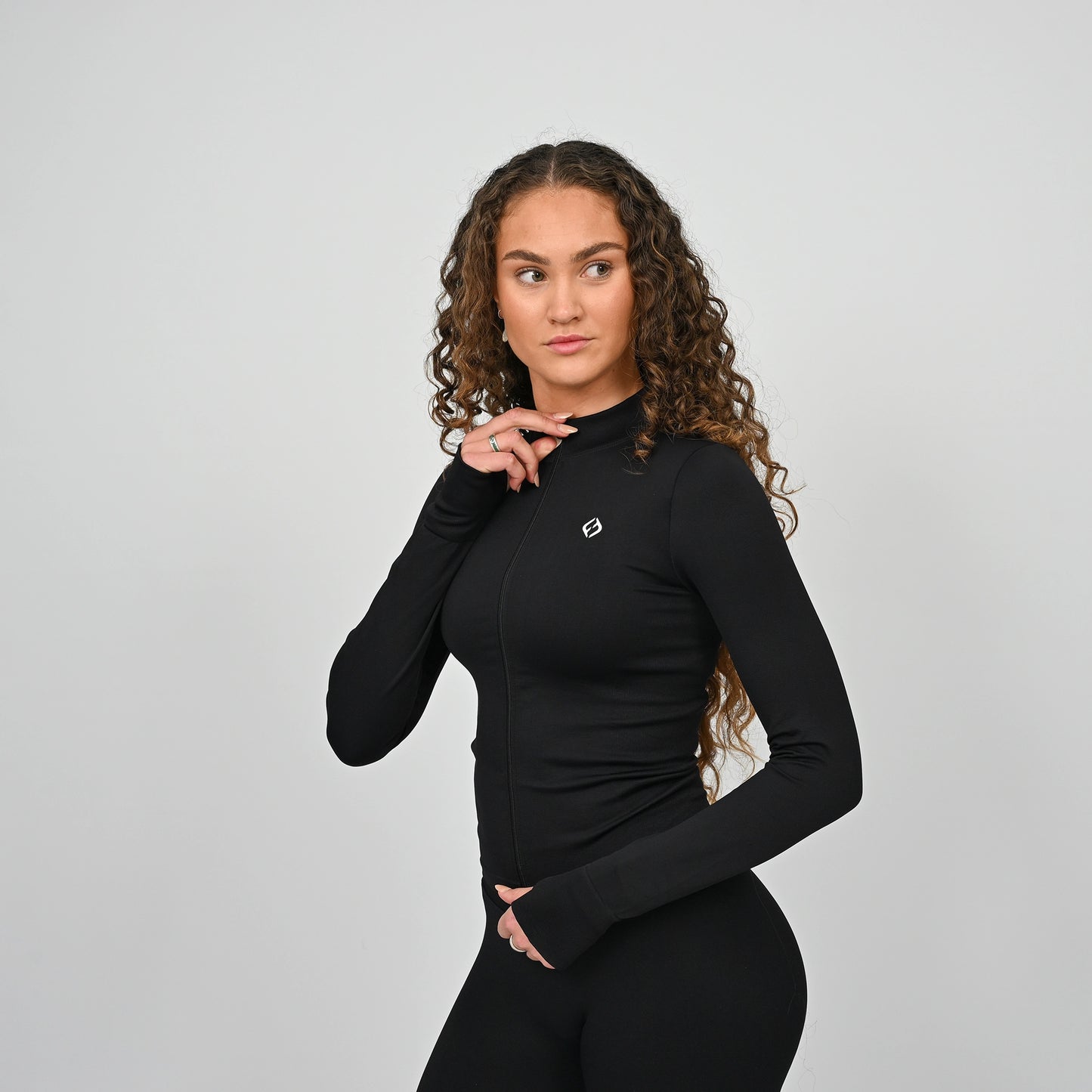 Woman wearing a black long-sleeve hybrid training top with a logo on a gray background