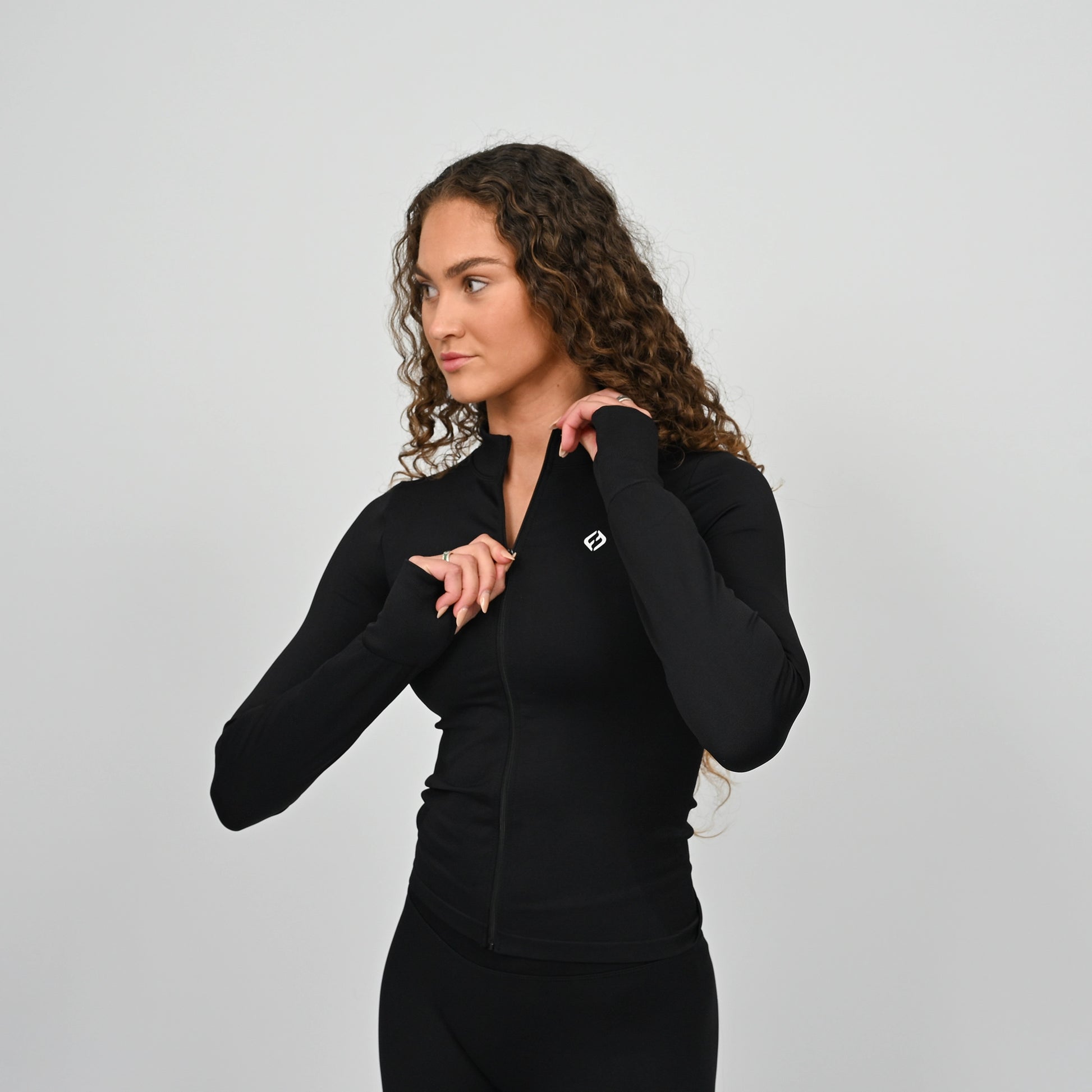 Woman wearing a black matching set training outfit with a Hybryd logo on a light gray background