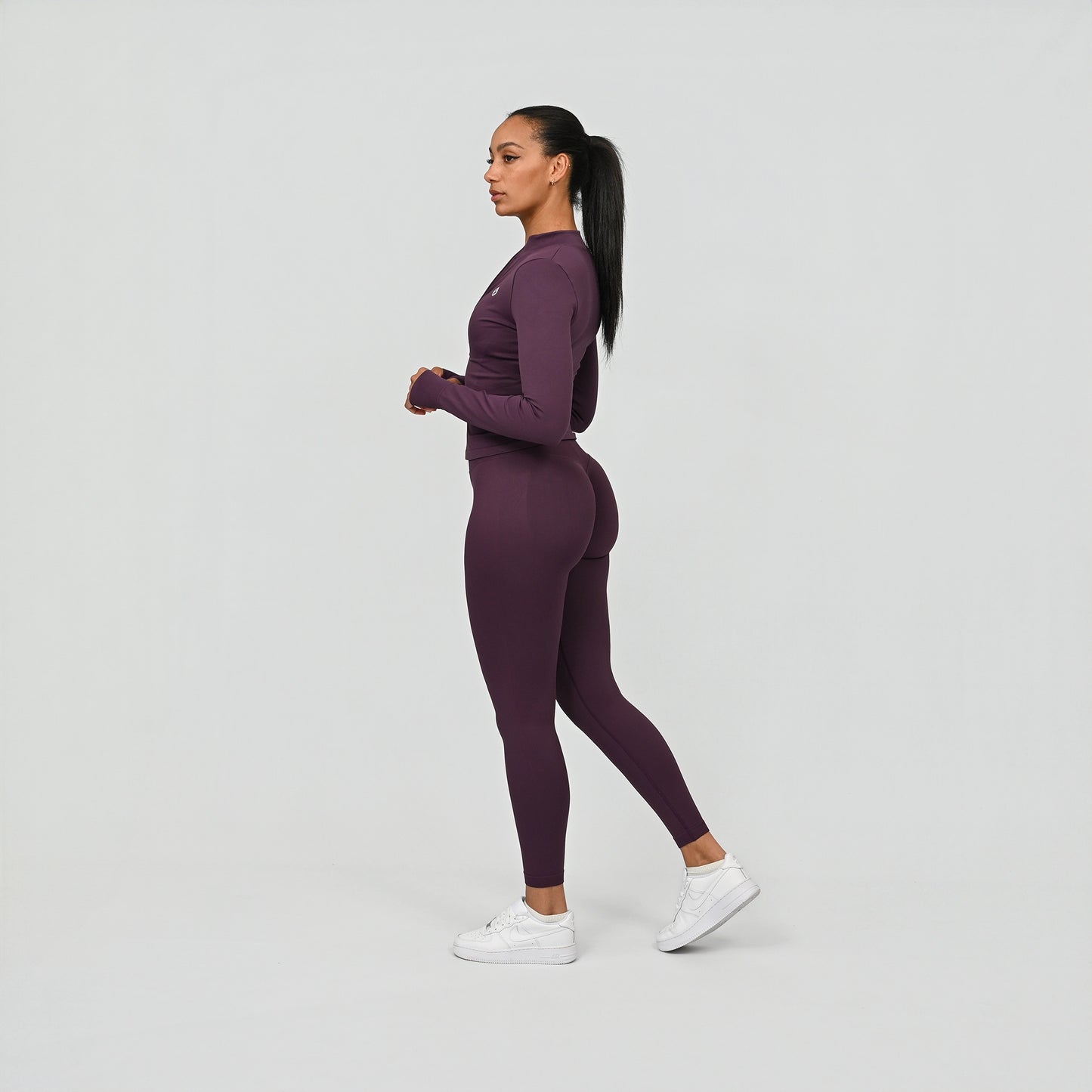 Woman wearing a purple long sleeve jacket and leggings outfit on a white background