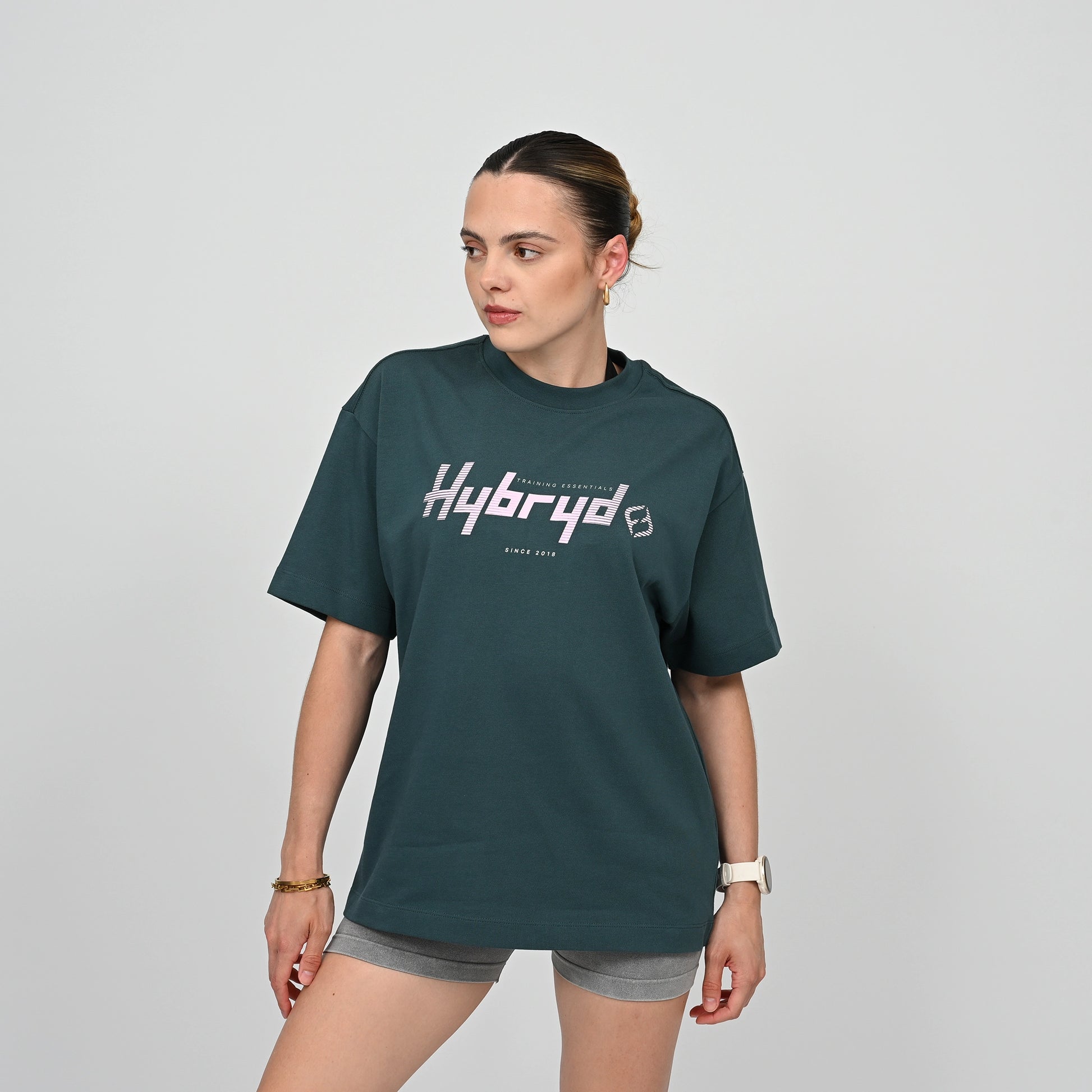 Woman wearing a green unisex t-shirt with 'Hybryd' logo on a gray background