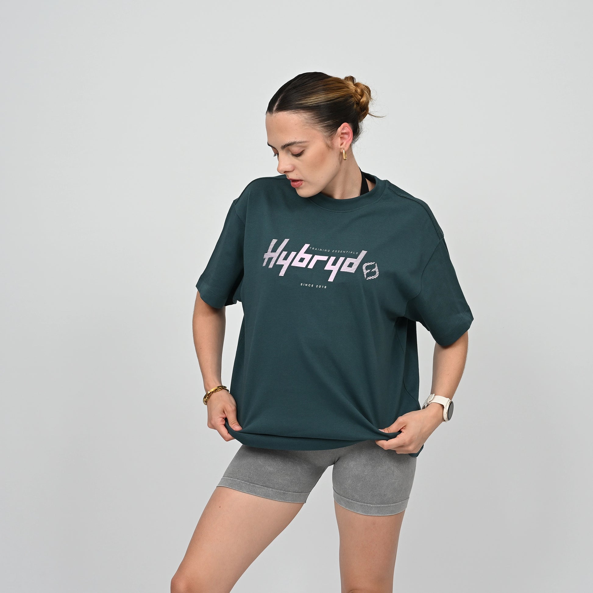 Woman wearing a green 'Hybryd' t-shirt and gray shorts on a light gray background
