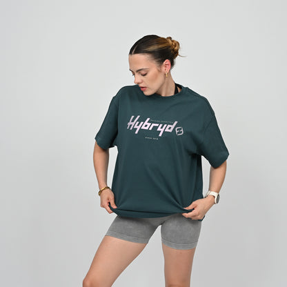 Woman wearing a green 'Hybryd' t-shirt and gray shorts on a light gray background
