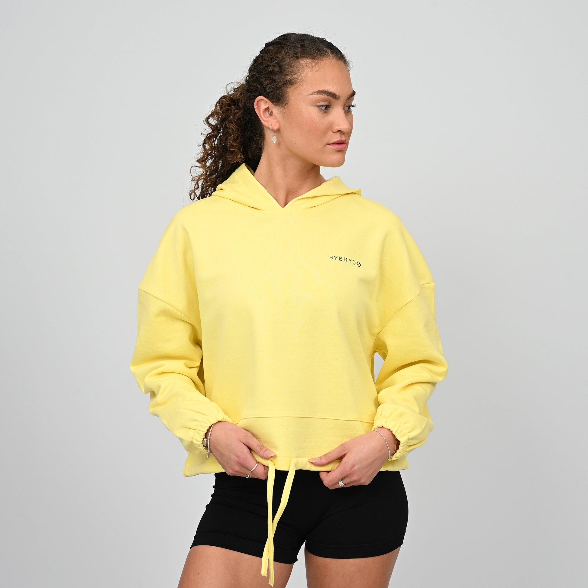 Woman wearing a yellow hoodie with a Hybryd brand logo on a grey background