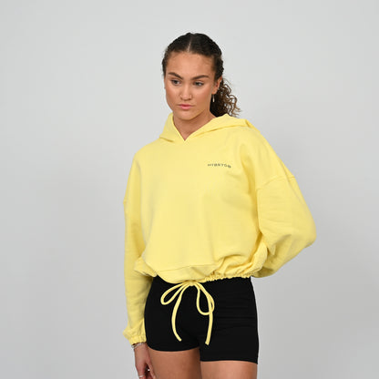 Person wearing a yellow hoodie and black shorts from Hybryd on a grey background