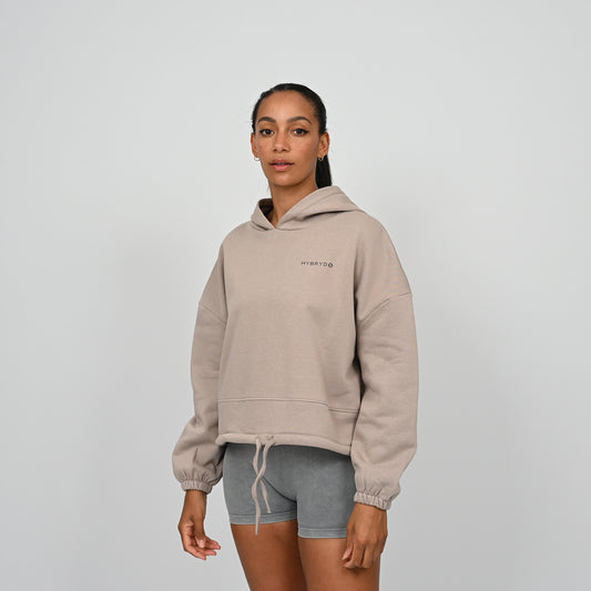 Person wearing a beige oversized hoodie with a Hybryd logo on a plain background