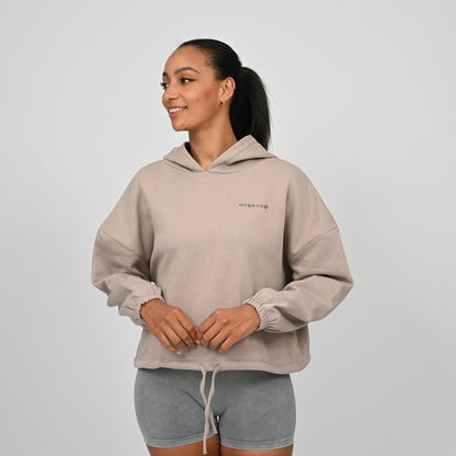 Woman wearing a beige hoodie with a Hybryd logo on a light gray background