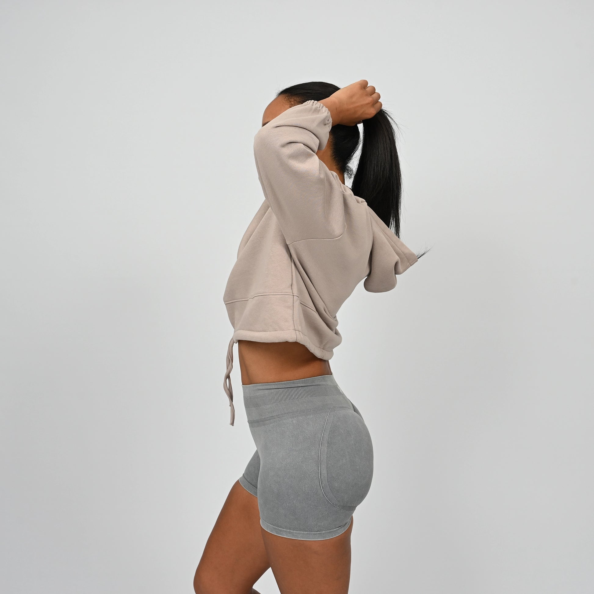 Person wearing a cropped post training hoodie with drawstring and grey scrunch bum shorts