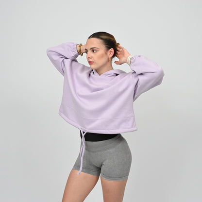Woman wearing a light purple hoodie from Hybryd and grey booty shorts on a plain background