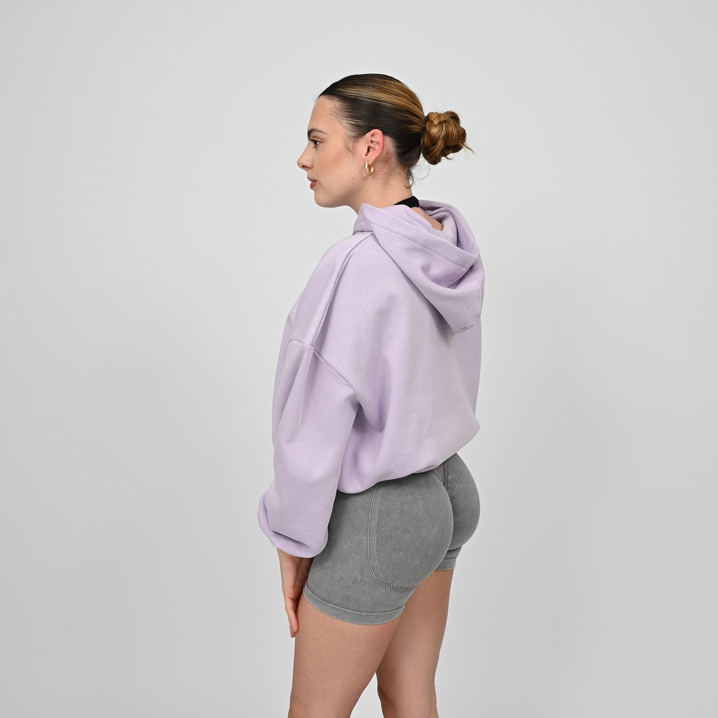 Woman wearing a lavender hoodie and gray shorts on a light gray background. From gymwear brand Hybryd