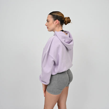 Woman wearing a lavender hoodie and gray shorts on a light gray background. From gymwear brand Hybryd