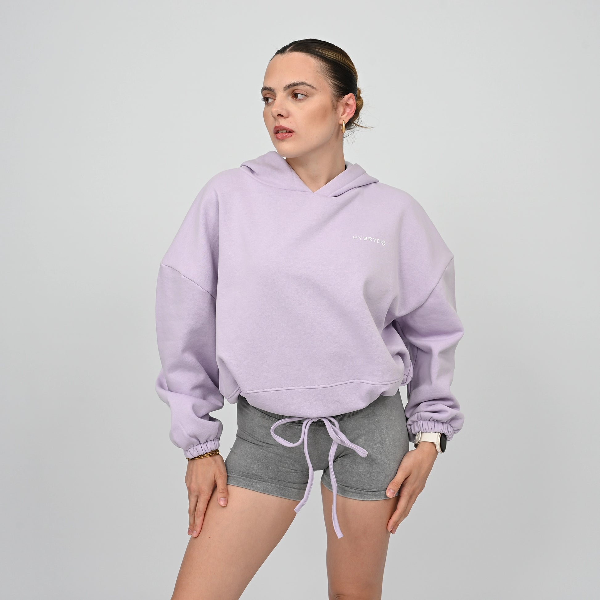 Woman wearing a light purple hoodie and grey Hybryd shorts on a plain background