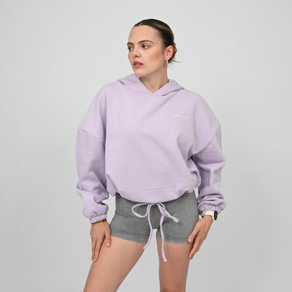 Woman wearing a light purple hoodie and grey Hybryd shorts on a plain background