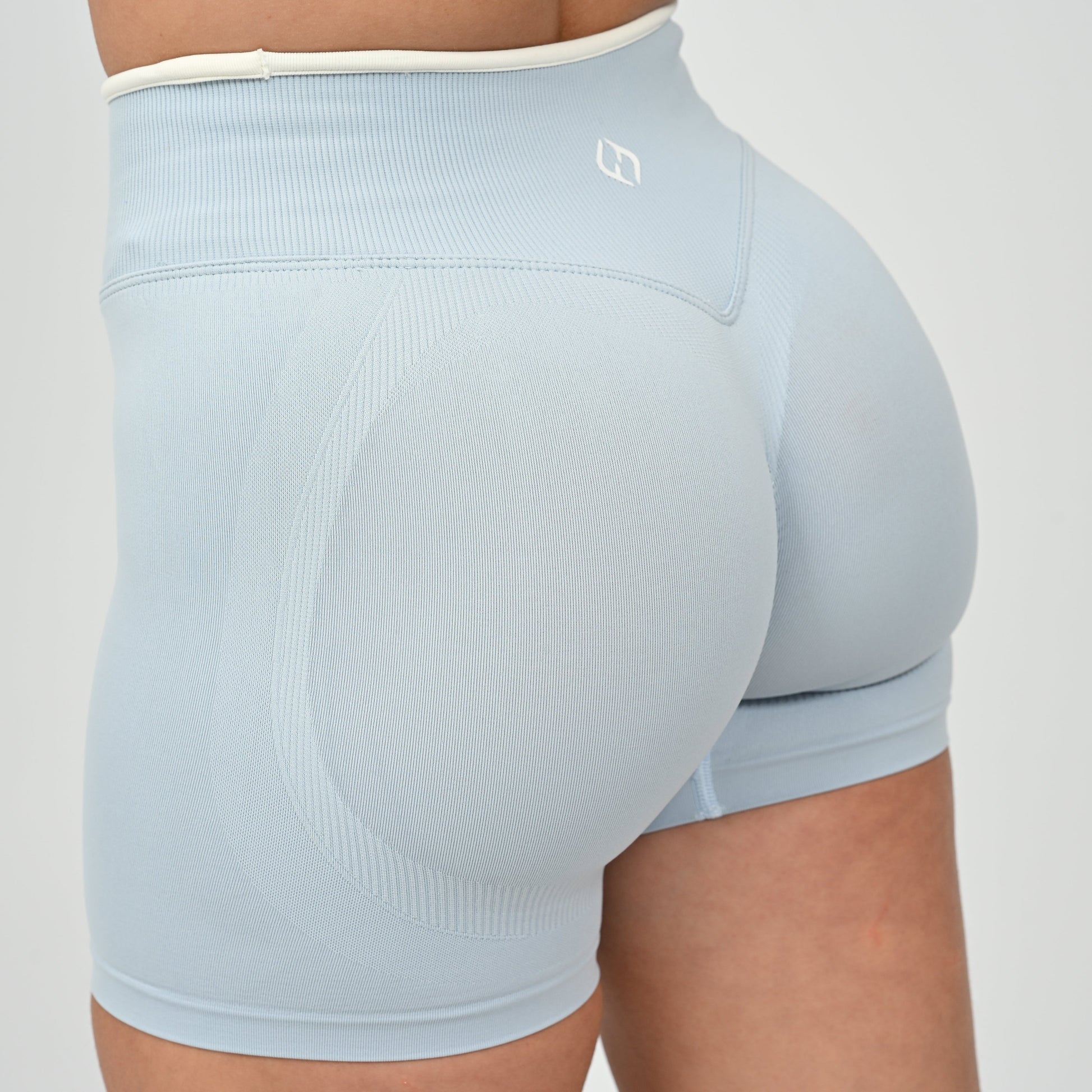Hyrox athlete wearinga pair of powder blue booty shorts with white piping. High waisted with a cinch bum and contouring.  From the brand Hybryd.