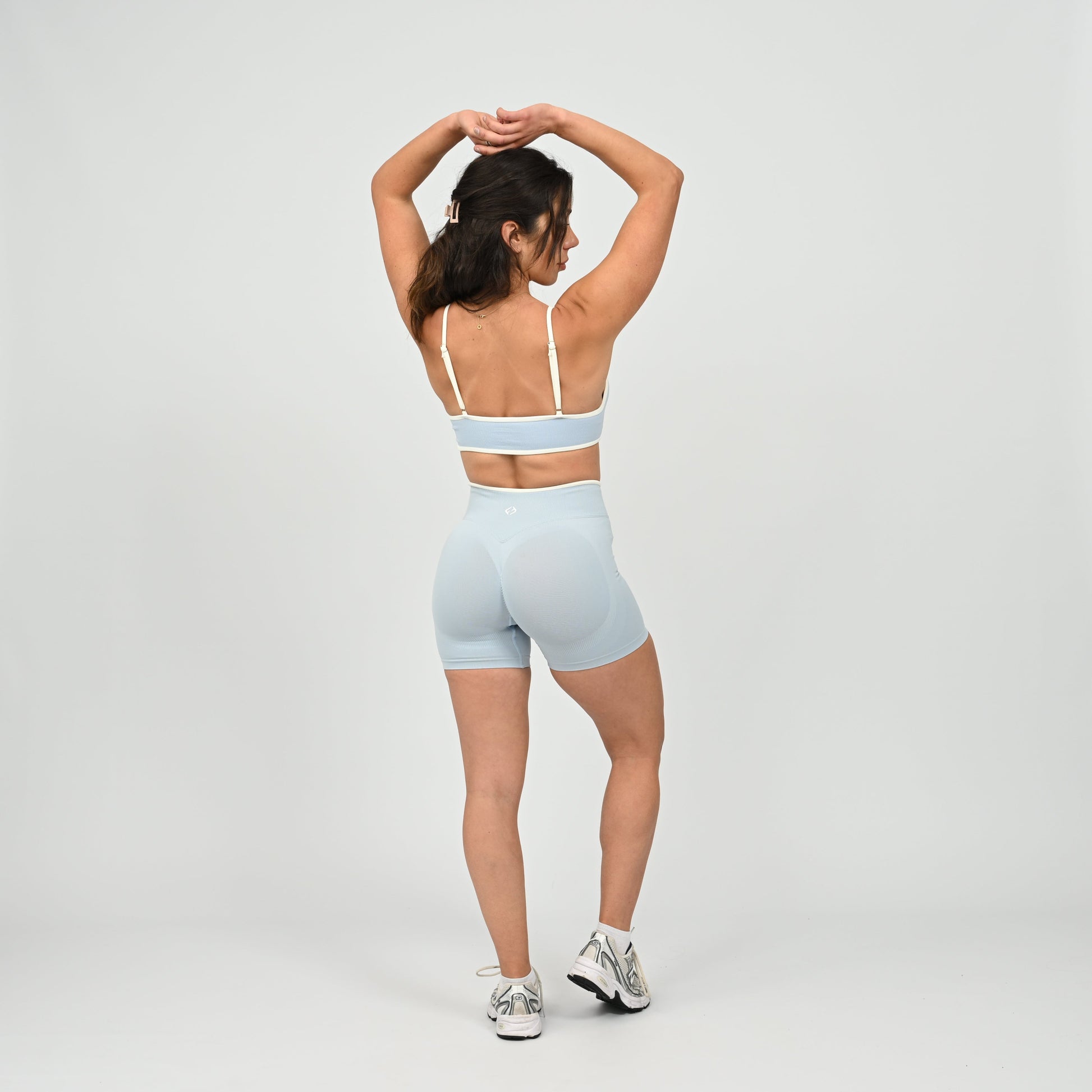 Hyrox athlete wearinga pair of powder blue booty shorts with white piping. High waisted with a cinch bum and contouring. Worn with a matching minimal sports bra. From the brand Hybryd.
