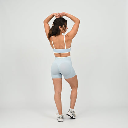 Hyrox athlete wearinga pair of powder blue booty shorts with white piping. High waisted with a cinch bum and contouring. Worn with a matching minimal sports bra. From the brand Hybryd.