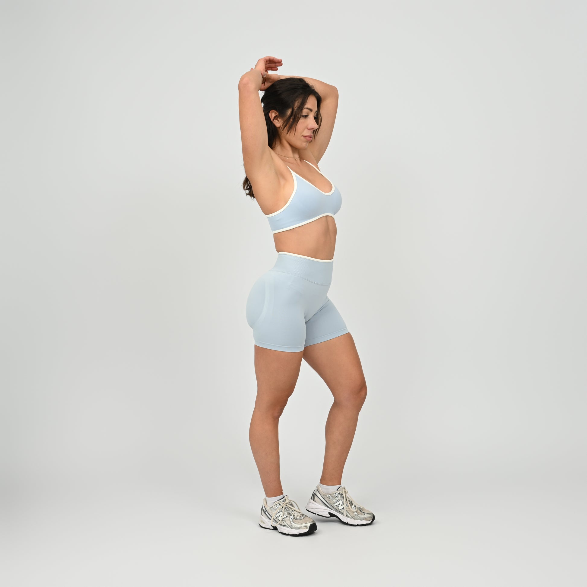 Hyrox athlete wearinga pair of powder blue booty shorts with white piping. High waisted with a cinch bum and contouring. Worn with a matching minimal sports bra. From the brand Hybryd.