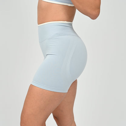 Hyrox athlete wearinga pair of powder blue booty shorts with white piping. High waisted with a cinch bum and contouring. Worn with a matching minimal sports bra. From the brand Hybryd.