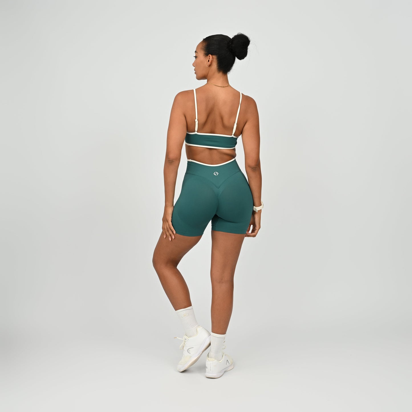 Hyrox athlete wearinga pair of Jade green booty shorts with white piping. High waisted with a cinch bum and contouring. Worn with a matching minimal sports bra. From the brand Hybryd.